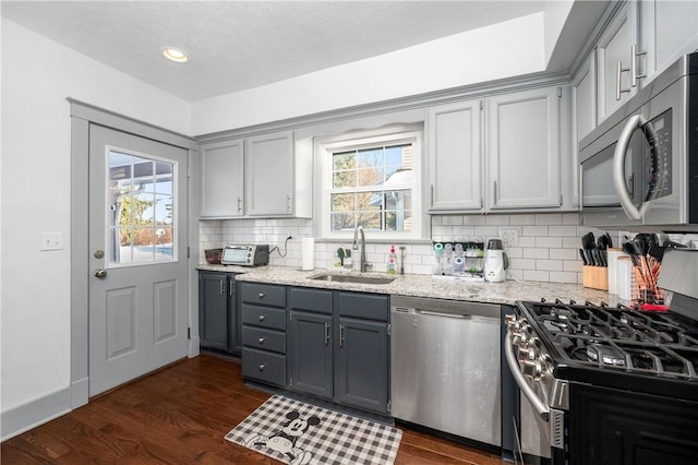 kitchen with sink, dark hardwood / wood-style floors, light stone countertops, gray cabinetry, and appliances with stainless steel finishes