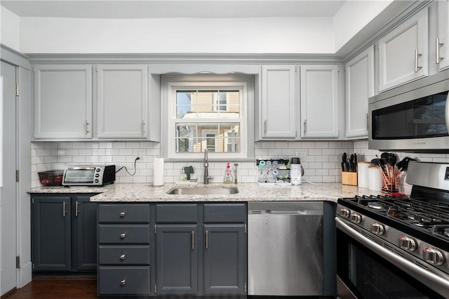 kitchen featuring gray cabinets, stainless steel appliances, light stone countertops, decorative backsplash, and sink