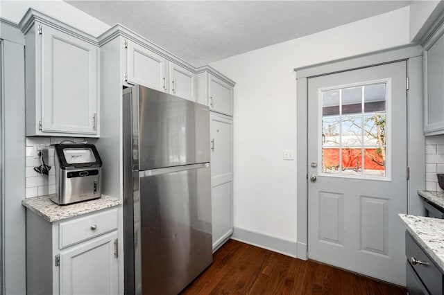 kitchen featuring dark hardwood / wood-style flooring, light stone countertops, stainless steel fridge, and tasteful backsplash