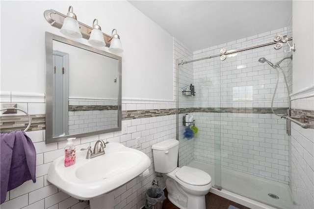 bathroom featuring tile walls, a shower with door, sink, and toilet