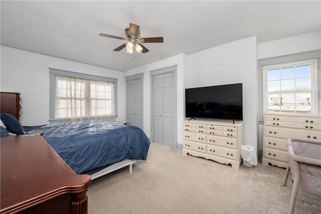 carpeted bedroom featuring ceiling fan and multiple closets