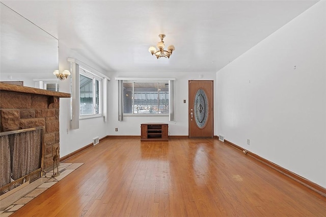 unfurnished living room featuring a stone fireplace, a chandelier, and wood-type flooring