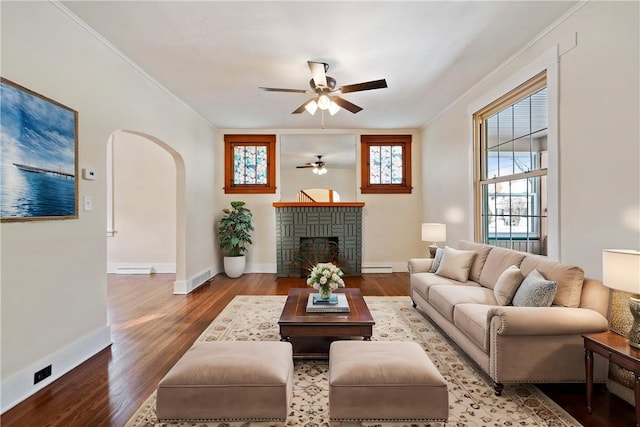 living room featuring a fireplace, ornamental molding, ceiling fan, wood-type flooring, and a baseboard radiator