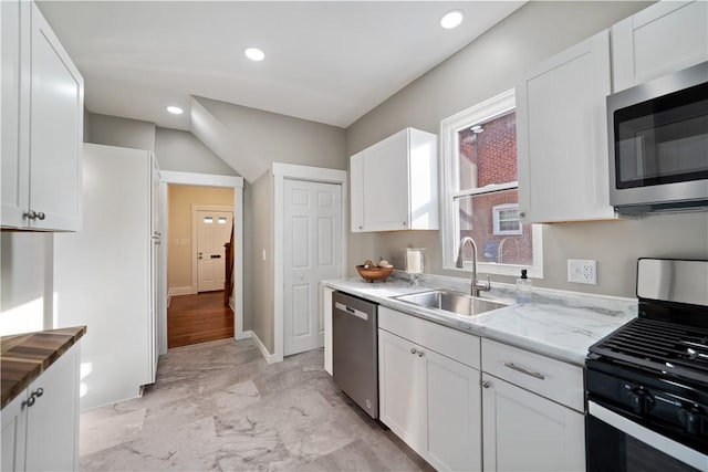 kitchen with stainless steel appliances, white cabinetry, sink, and light stone counters