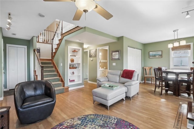 living room featuring built in shelves, track lighting, ceiling fan, and light hardwood / wood-style flooring