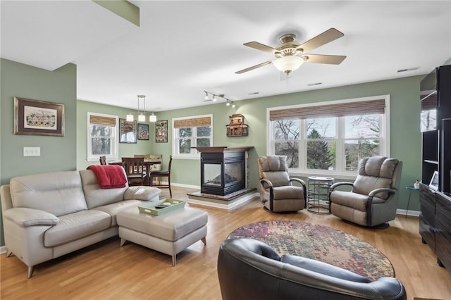 living room featuring a multi sided fireplace, rail lighting, ceiling fan, and light hardwood / wood-style flooring