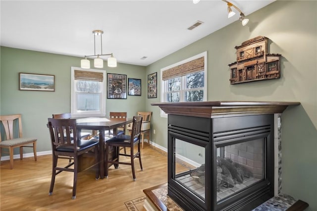 dining room with light hardwood / wood-style flooring, track lighting, and a multi sided fireplace