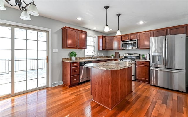 kitchen featuring stainless steel appliances, dark wood-type flooring, a kitchen island, sink, and decorative light fixtures