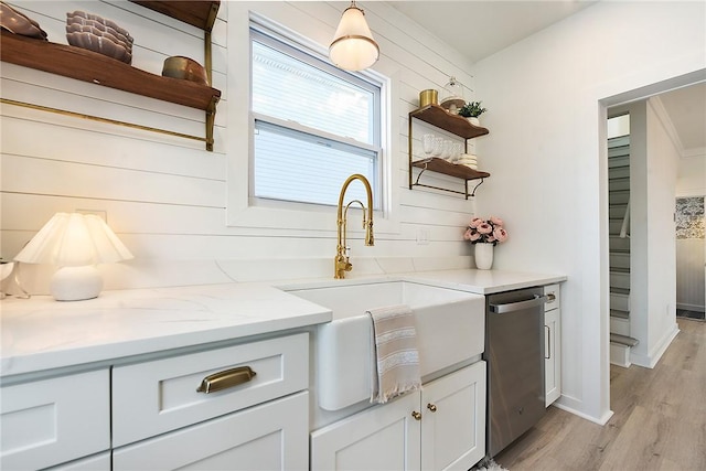 kitchen with sink, white cabinetry, light stone counters, light hardwood / wood-style flooring, and stainless steel dishwasher