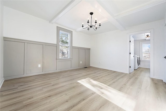 unfurnished dining area featuring washer and clothes dryer, a notable chandelier, light wood-type flooring, plenty of natural light, and beamed ceiling