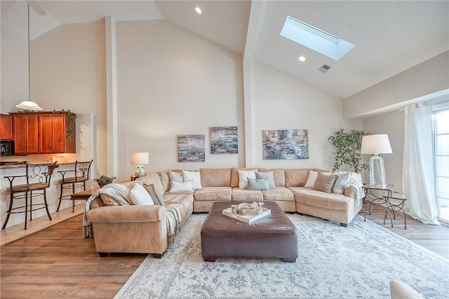 living room with light hardwood / wood-style floors, a skylight, and high vaulted ceiling