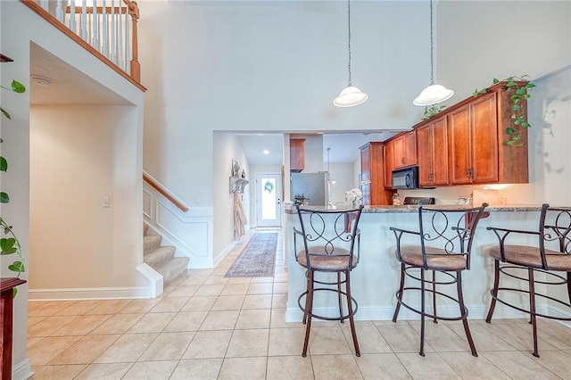 kitchen featuring stainless steel fridge, light tile patterned flooring, a towering ceiling, and hanging light fixtures