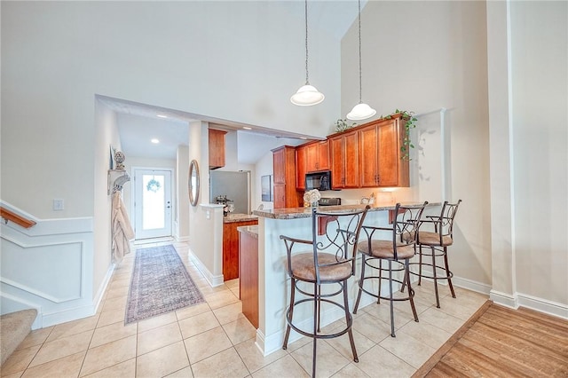 kitchen with decorative light fixtures, high vaulted ceiling, kitchen peninsula, and light tile patterned floors