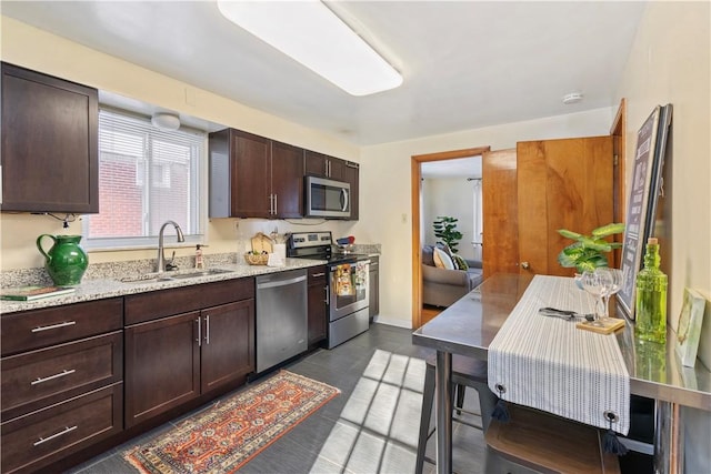 kitchen with sink, dark brown cabinets, light stone counters, and appliances with stainless steel finishes