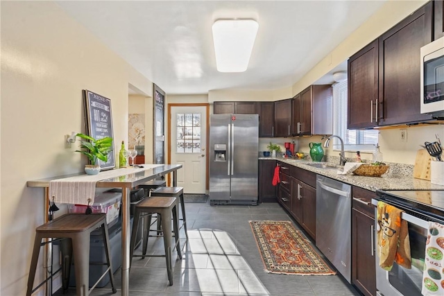 kitchen featuring light stone countertops, a kitchen bar, appliances with stainless steel finishes, dark brown cabinets, and sink