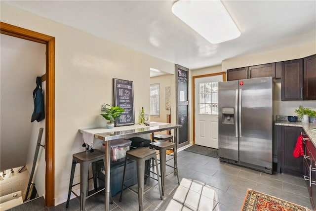 kitchen featuring stainless steel refrigerator with ice dispenser, a kitchen breakfast bar, and dark brown cabinetry