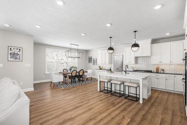 kitchen featuring decorative light fixtures, a breakfast bar area, white cabinets, decorative backsplash, and a kitchen island with sink