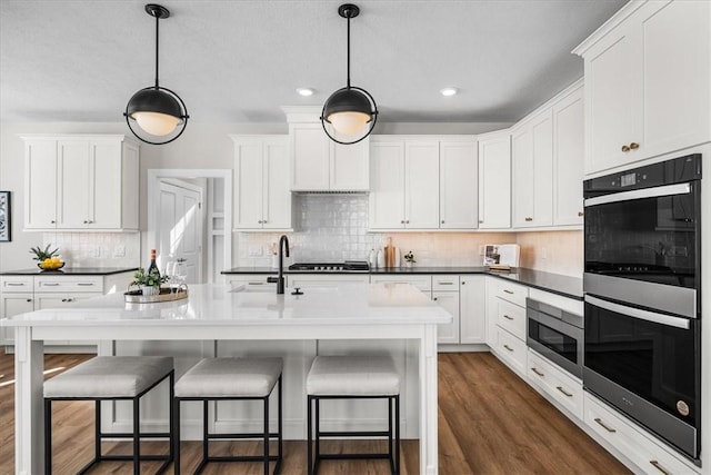 kitchen featuring sink, white cabinetry, hanging light fixtures, multiple ovens, and dark hardwood / wood-style flooring