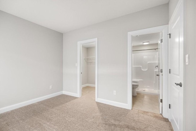 unfurnished bedroom featuring ensuite bathroom, a spacious closet, light colored carpet, and a closet