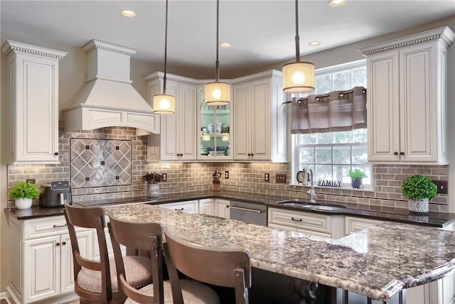 kitchen featuring decorative light fixtures, dishwasher, dark stone countertops, decorative backsplash, and custom range hood