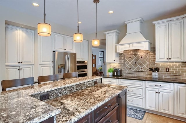 kitchen featuring pendant lighting, white cabinets, decorative backsplash, stainless steel appliances, and custom range hood