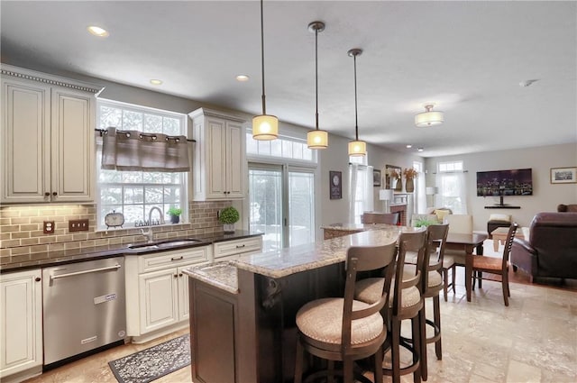 kitchen with dishwasher, sink, backsplash, dark stone counters, and hanging light fixtures