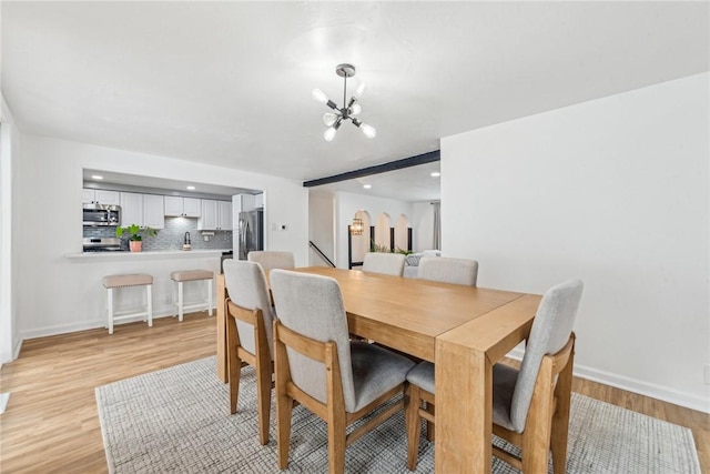 dining room featuring beam ceiling, light hardwood / wood-style flooring, and a chandelier