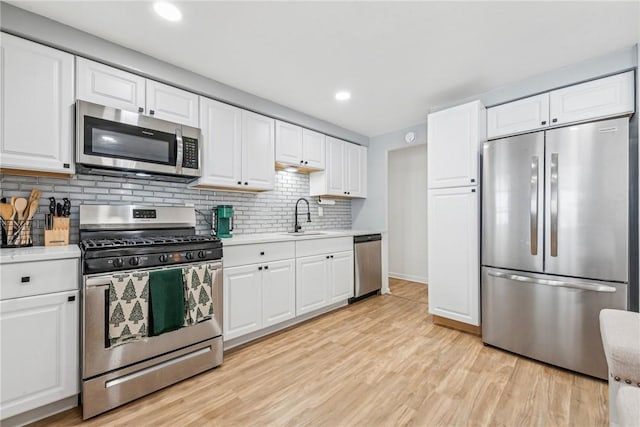 kitchen with stainless steel appliances, sink, white cabinets, light hardwood / wood-style floors, and backsplash