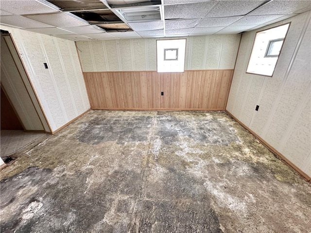 basement with a paneled ceiling, wooden walls, and plenty of natural light