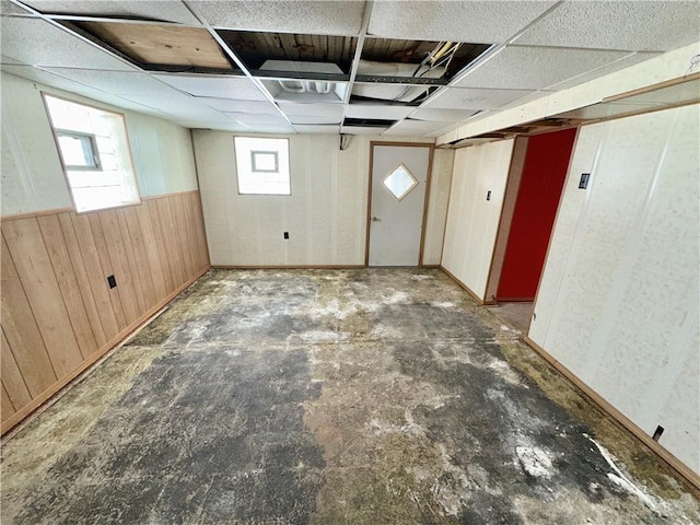 basement featuring wood walls and a drop ceiling