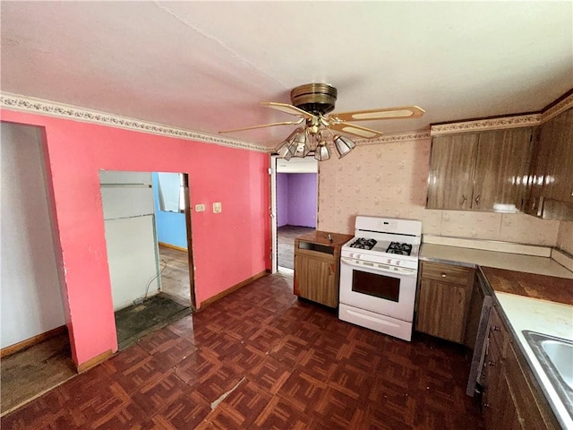 kitchen with sink, dark parquet flooring, white gas range oven, and ceiling fan