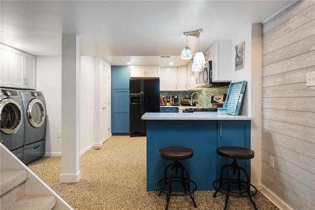 kitchen with washing machine and dryer, wooden walls, white cabinets, black refrigerator with ice dispenser, and stove