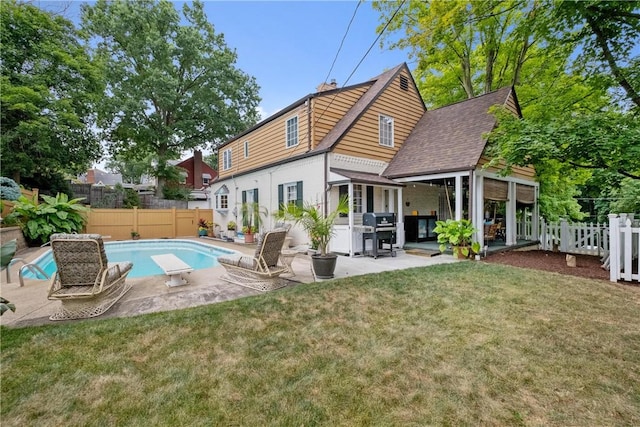 rear view of property featuring a patio, a yard, and a fenced in pool