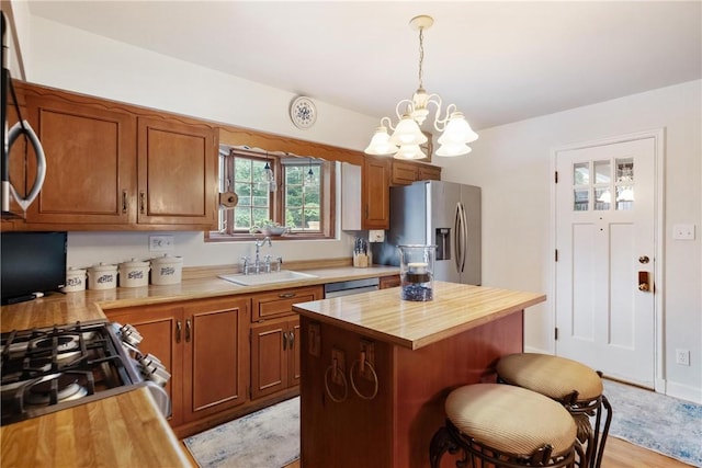 kitchen with sink, decorative light fixtures, a center island, wood counters, and appliances with stainless steel finishes