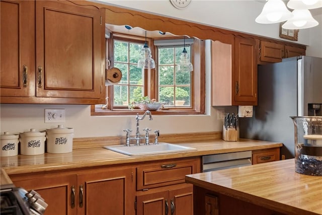 kitchen with sink, dishwasher, wooden counters, stainless steel refrigerator with ice dispenser, and pendant lighting