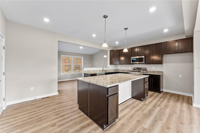 kitchen featuring appliances with stainless steel finishes, hanging light fixtures, light stone counters, sink, and dark brown cabinets