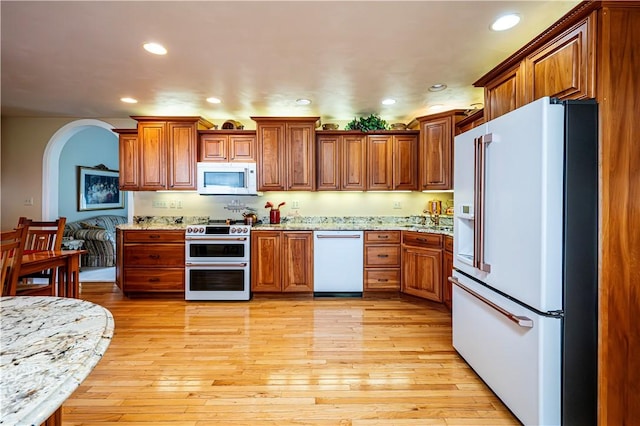 kitchen featuring white appliances, light wood-type flooring, and light stone counters