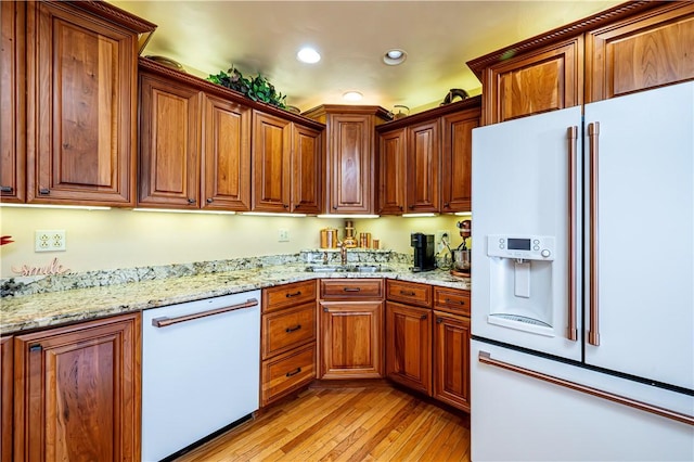 kitchen with sink, white appliances, light hardwood / wood-style floors, and light stone counters