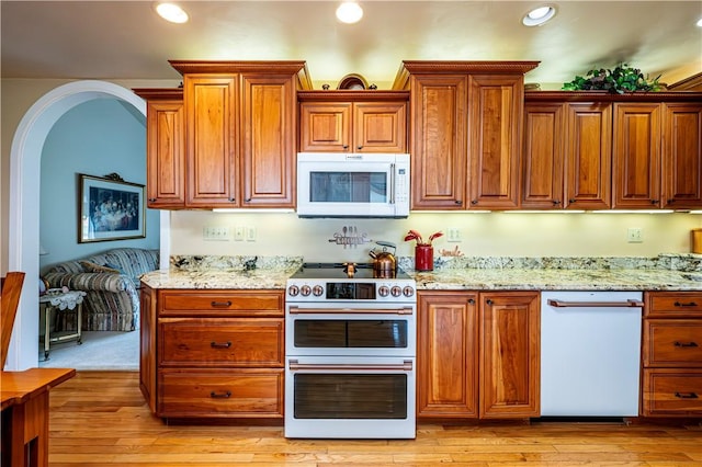 kitchen with white appliances, light wood-type flooring, and light stone counters