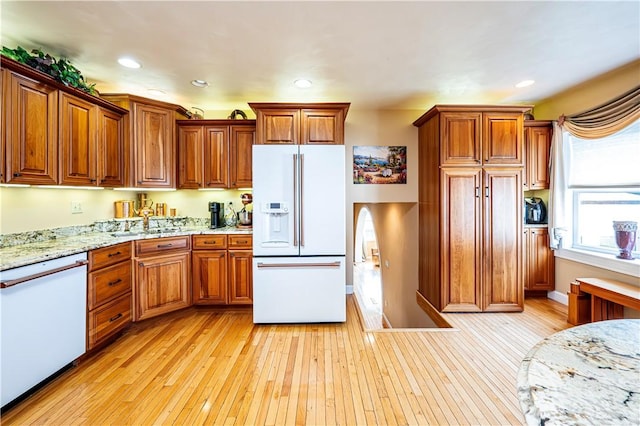 kitchen with white appliances, light wood-type flooring, and light stone counters