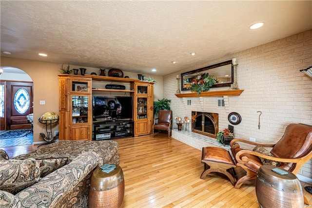 living room with a textured ceiling, light wood-type flooring, a brick fireplace, and brick wall