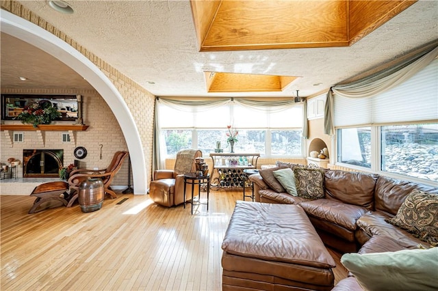 interior space with a textured ceiling, a fireplace, a raised ceiling, light hardwood / wood-style floors, and a skylight