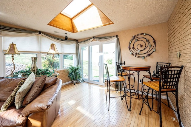 interior space with light hardwood / wood-style floors, a skylight, a textured ceiling, and brick wall