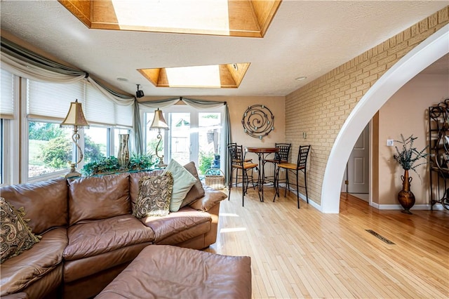 living room with brick wall, a textured ceiling, a skylight, and light hardwood / wood-style flooring