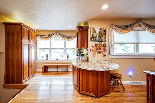 kitchen featuring light stone countertops, light wood-type flooring, and a kitchen breakfast bar