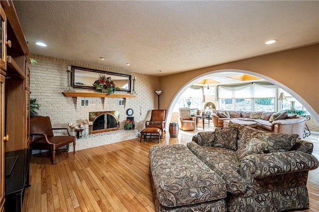 living room with brick wall, a fireplace, hardwood / wood-style floors, and a textured ceiling