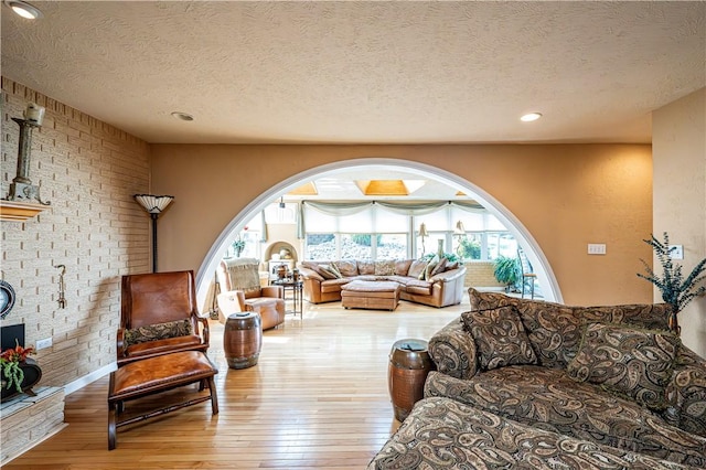 living room with brick wall, a brick fireplace, a textured ceiling, and light wood-type flooring