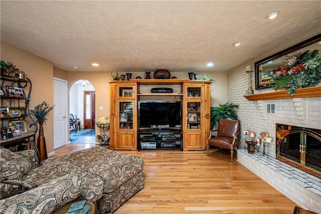 living room with a textured ceiling, a fireplace, and light hardwood / wood-style flooring