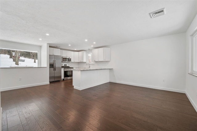 kitchen with kitchen peninsula, light stone countertops, stainless steel appliances, dark hardwood / wood-style flooring, and white cabinets