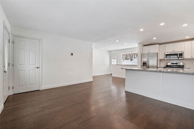 kitchen with light stone countertops, white cabinets, dark hardwood / wood-style floors, and appliances with stainless steel finishes